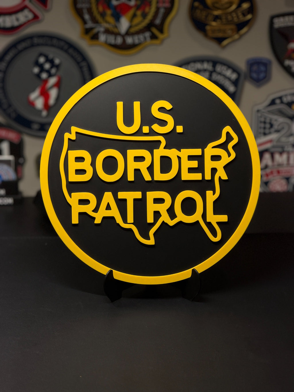 Round U.S. Border Patrol 3D printed plaque in black and yellow, displayed on a stand